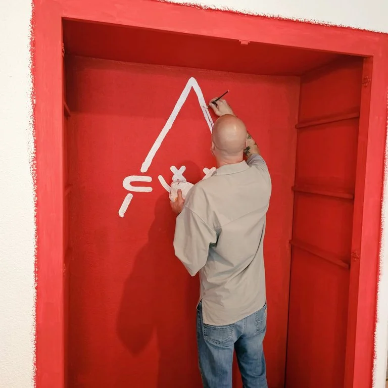 Skeenee painting the Crypto Art symbol on a red wall.